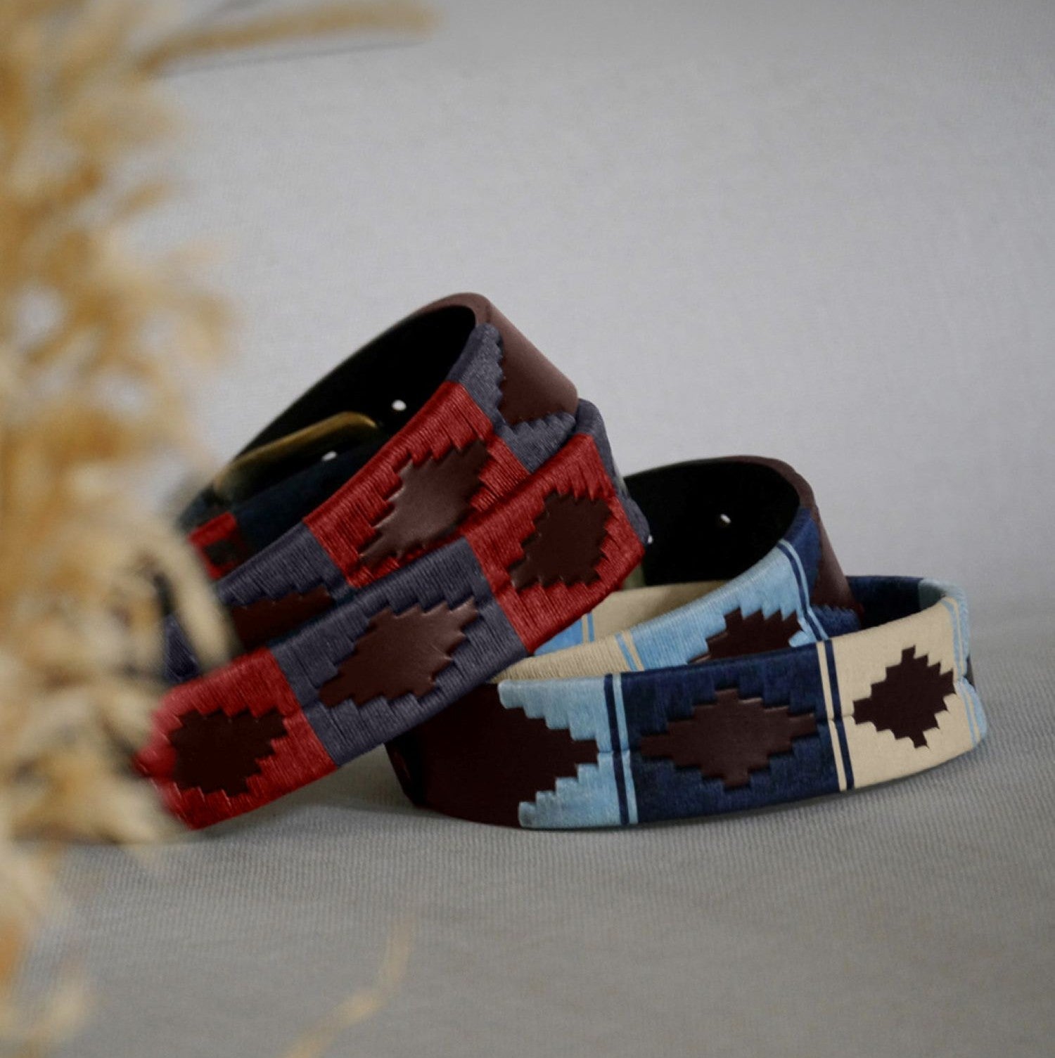 Two pampeano full-grain leather belts for men and women in red, navy, blue and cream, displayed on a table